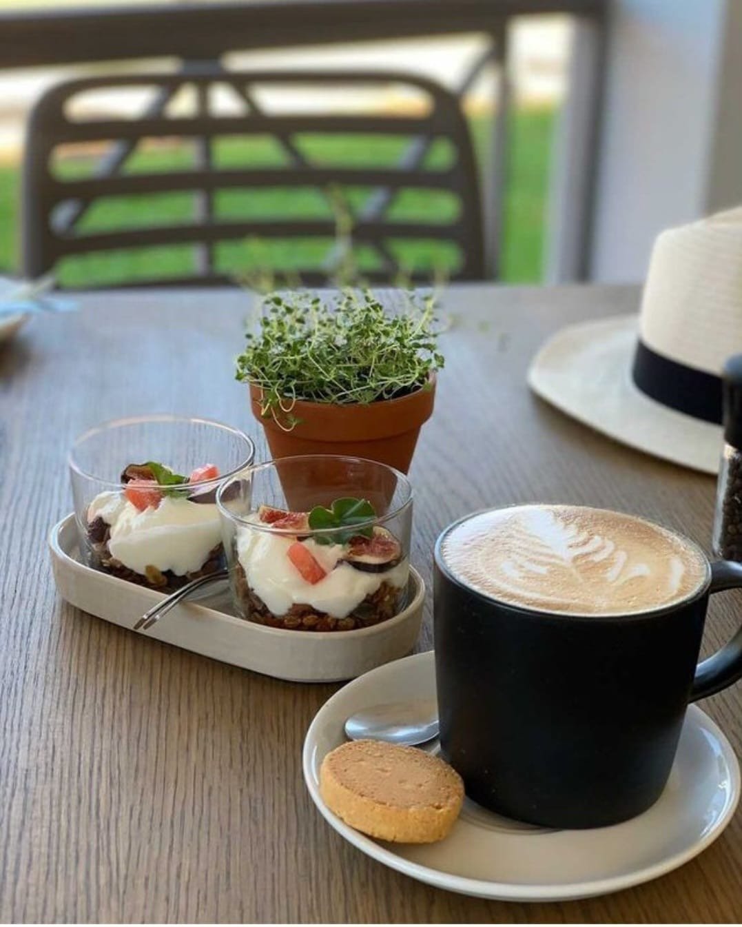 A cappuccino beside two granola and yoghurt pots with fresh fruit