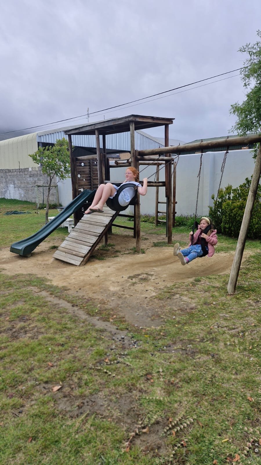 Two children on the swings in the fenced play area